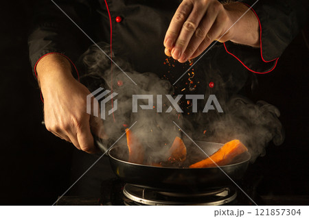 In a warm kitchen, skilled hands sprinkle aromatic spices into a pan of brightly colored vegetables. The rising steam and rich colors create a tantalizing atmosphere of culinary creativity 121857304