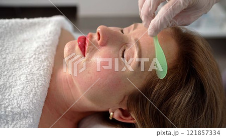 A female cosmetologist doctor applies a gel on the face of a young woman. Applying gel on the face in a beauty parlor. A female cosmetologist doctor applies a gel on the face of a young woman. Applying gel on the face in a beauty parlor. 121857334