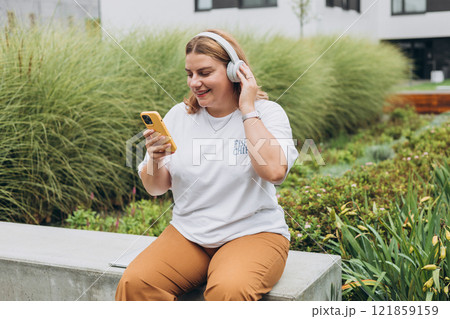 Closeup portrait of a lovely young female listening to music through wireless earphones on urban background. Music lover enjoying music. Woman record voice by mobile cell phone Dictaphone 121859159