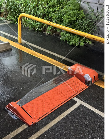 Wet parking lot barrier with reflective orange ramp. Concept of traffic management, urban infrastructure, and safety measures. 121861013
