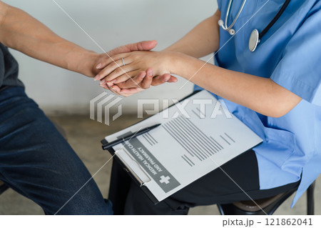 A nurse offers reassuring care by holding a patient's hand during a medical consultation, creating a supportive and empathetic atmosphere. A nurse offers reassuring care by holding a patient's hand during a medical consultation, creating a supportive and empathetic atmosphere. 121862041