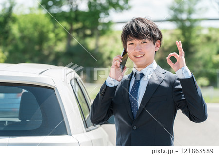 車の前でスマホで通話するスーツ姿の若いアジア人ビジネスマン 121863589