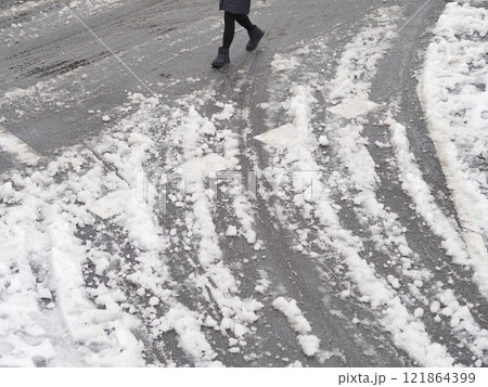 積雪した道路を歩く人と複数のタイヤ跡 121864399