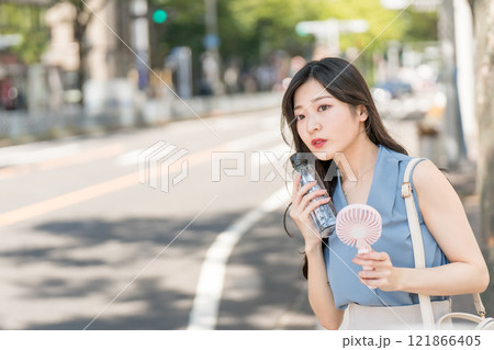 ハンディファンとペットボトルの水を持って木陰で涼むビジネスウーマン 121866405