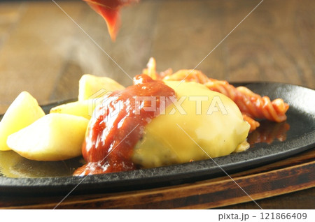 とろけるチーズをまとったハンバーグにたっぷりのトマトソースをかけ、ポテトとパスタを添えた鉄板仕上げ 121866409