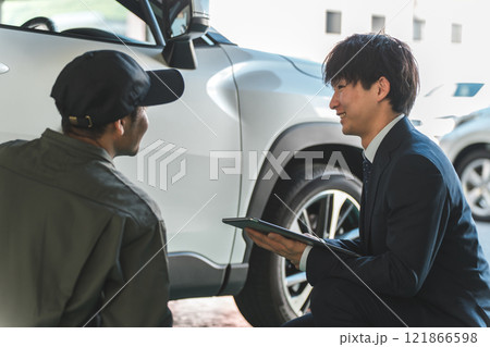 自動車の前で会話する自動車整備士の男性とスーツ姿のフロントマン・営業マン 自動車の前で会話する自動車整備士の男性とスーツ姿のフロントマン・営業マン 121866598