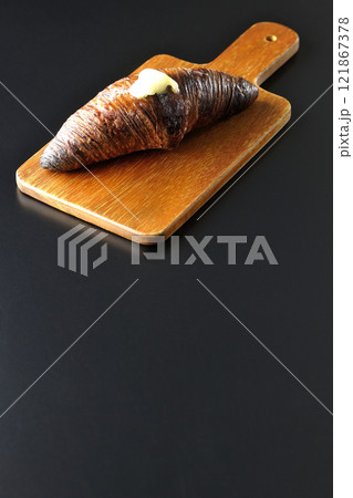 カッティングボードに乗ったちょっと焦げてる黒ワッサンを黒背景で撮影 カッティングボードに乗ったちょっと焦げてる黒ワッサンを黒背景で撮影 121867378