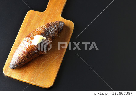 カッティングボードに乗ったちょっと焦げてる黒ワッサンを黒背景で撮影 121867387