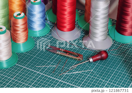 Multi-colored bobbins with threads for stitching leather and tanners tools on a cutting mat, selected focus. 121867731