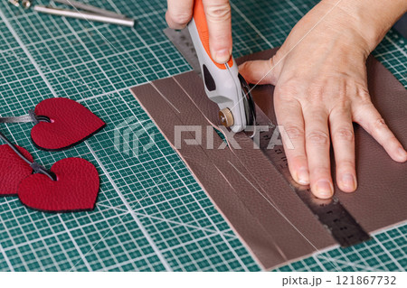 Tanners hands cut leather using work tool on a green cutting mat, close-up, process. Tanners hands cut leather using work tool on a green cutting mat, close-up, process. 121867732