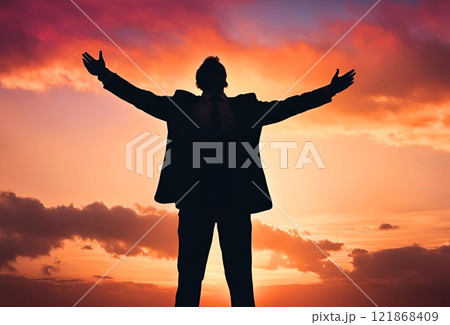 夕焼け空をバックに両手を広げているビジネスマンのシルエット 121868409