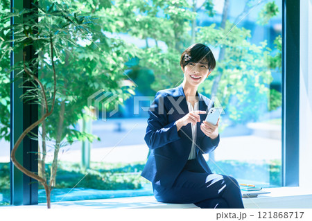 オフィスでスマホを操作するスーツ姿のミドルビジネスウーマン撮影協力：LINK FOREST 121868717