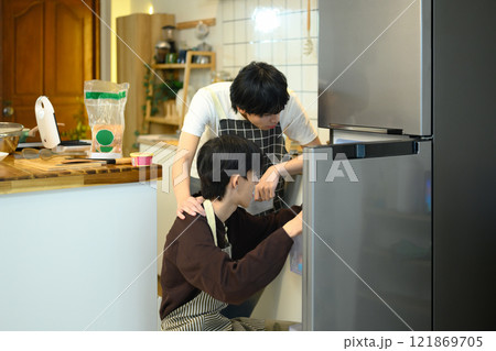 Loving gay couple preparing breakfast in their cozy kitchen while searching for ingredients in the fridge 121869705