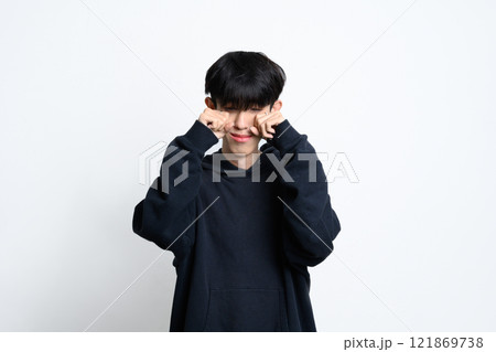 Young man in black hoodie crying and wiping tears over white background 121869738