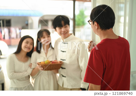 Cheerful family arriving at a relative home during Chinese New Year, carrying a basket of fruits as a gift 121869740