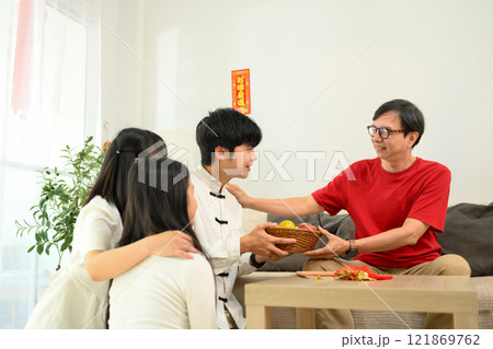Family gathering during Chinese New Year giving basket of fruits to elder parent symbolizing respect and gratitude 121869762