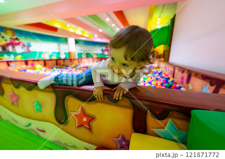 A playful child climbing over a colorful wall in a vibrant indoor playground. 121871772