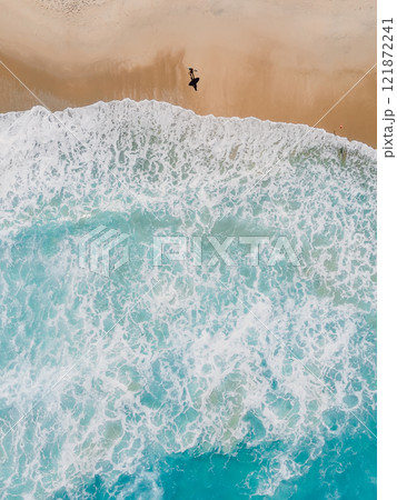 Surfer walks on sandy beach with ocean and waves. Aerial view, top down 121872241