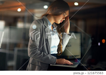 Stressed, worried and tired female entrepreneur typing on a laptop and working overtime late at night. Frustrated and overworked young businesswoman with a headache doing a project with a deadline 121875563