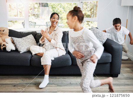 Playing, running and young children excited indoors with a smiling mother watching on a couch. Happy family spending the day together indoors while the active kids run, play and have fun at home 121875650