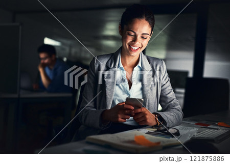 Woman reading text late on phone, smiling at a message and looking at social media posts online while working in a dark office at night. Happy corporate worker checking emails and doing overtime Woman reading text late on phone, smiling at a message and looking at social media posts online while working in a dark office at night. Happy corporate worker checking emails and doing overtime 121875886