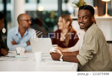 Proud, happy and smiling young businessman holding digital tablet during business meeting. Ambitious young businessperson with team or colleagues in office, sitting in a modern boardroom. 121875996