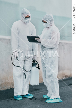 Healthcare workers cleaning outside a building using a list to follow instructions on biohazard safety during covid. Medical researchers wearing hazmat suits sanitizing outdoor to prevent infections 121876052