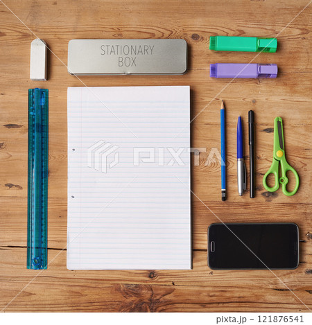 School supplies, stationary or equipment for young working and studying students top view. Assortment, variety or array of education essentials items including a phone and notebook on a wooden desk 121876541