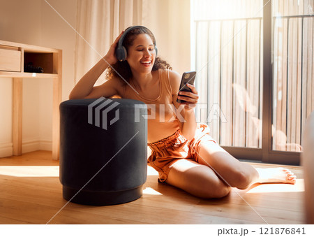 Carefree, relaxed and happy woman relaxing on a video call using her phone and headphones while sitting on the floor. A young excited female listening to an online podcast or browsing social media 121876841