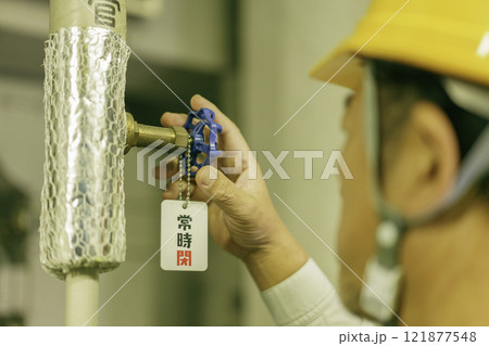 バルブを閉める男性作業員の手元のアップ　撮影協力：学校法人電波学園　東京電子専門学校 121877548