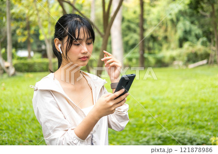 Young woman sitting and listening to music at the park. 121878986
