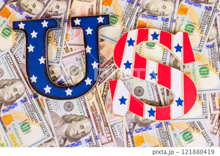 Letters US designed with stars, stripes rest atop pile of American hundred dollar bills, symbolizing finance. 121880419