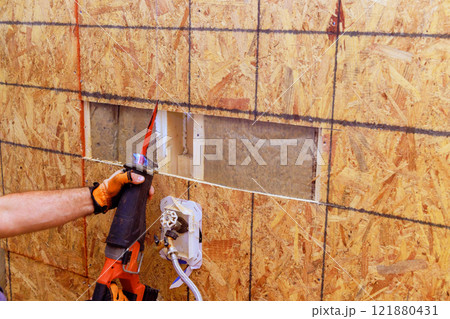 Contractor uses saw to cut through an oriented strand board wall for window installation in home renovation project. 121880431