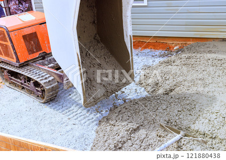 Wheelbarrow tracked machine pours fresh concrete onto prepared surface for new residential foundation under construction. Wheelbarrow tracked machine pours fresh concrete onto prepared surface for new residential foundation under construction. 121880438