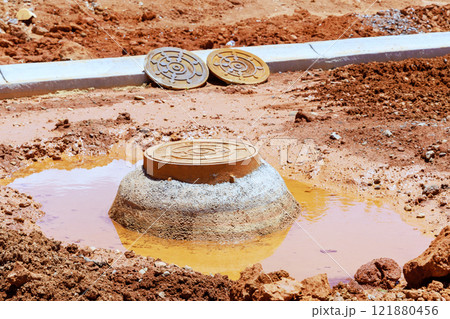 Drainage manhole stands in muddy soil, water, surrounded by construction site Drainage manhole stands in muddy soil, water, surrounded by construction site 121880456