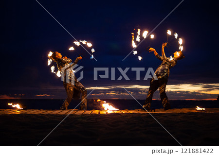 Two girls light a sparkler on the beach at dusk. 121881422