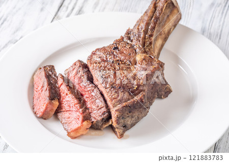 Sliced Grilled Medium-Rare Cowboy Steak on White Plate and Table Sliced Grilled Medium-Rare Cowboy Steak on White Plate and Table 121883783