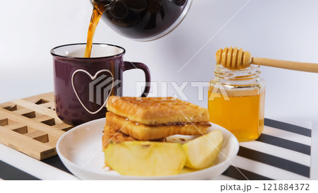 Fresh coffee poured into a mug with waffles, honey, and apples for a cozy breakfast Fresh coffee poured into a mug with waffles, honey, and apples for a cozy breakfast 121884372