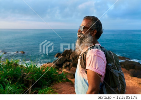 Senior man explores coastal cliffside, backpacking on scenic ocean hike. Elderly adventurer embraces nature, enjoys fresh sea breeze in twilight years. Multicultural hiker on outdoor travel journey. Senior man explores coastal cliffside, backpacking on scenic ocean hike. Elderly adventurer embraces nature, enjoys fresh sea breeze in twilight years. Multicultural hiker on outdoor travel journey. 121885178