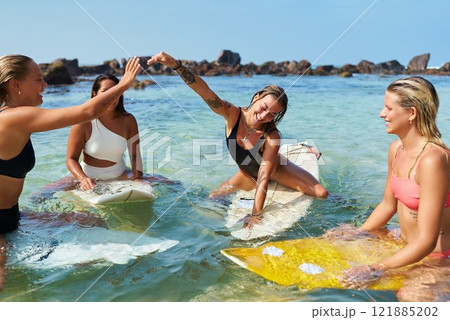 Four smiling women in swimwear on surfboards splash, laugh in shallow ocean water. Friends enjoy summer day, adventure. Happy teamwork vibe, unity with nature. Playful community spirit. Four smiling women in swimwear on surfboards splash, laugh in shallow ocean water. Friends enjoy summer day, adventure. Happy teamwork vibe, unity with nature. Playful community spirit. 121885202