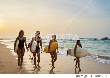 Four women walk on beach holding surfboards. Sunset sky, ocean waves, golden sand. Female surfers enjoy seaside, summer sport and leisure. Group of friends, fit lifestyle, coastal adventure. Four women walk on beach holding surfboards. Sunset sky, ocean waves, golden sand. Female surfers enjoy seaside, summer sport and leisure. Group of friends, fit lifestyle, coastal adventure. 121885204