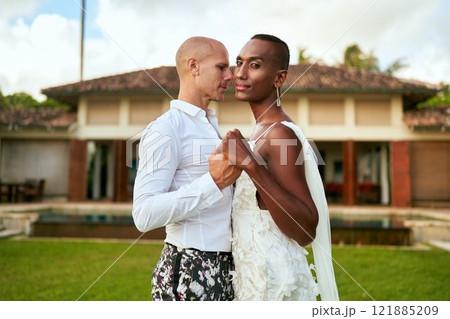 LGBTQ wedding at tropical villa. Ambiguous gender fluid bride in white dress, groom in bold suit dance. Elegant couple in vibrant love story. Inclusive, diverse celebration. Modern wedding. 121885209