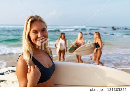 Group of women with surfboards on sunny beach. Friends enjoy surfing, ocean waves, summer fun. Young females in swimsuits relax near sea. Active lifestyle, female surfers, beach vacation. Group of women with surfboards on sunny beach. Friends enjoy surfing, ocean waves, summer fun. Young females in swimsuits relax near sea. Active lifestyle, female surfers, beach vacation. 121885255