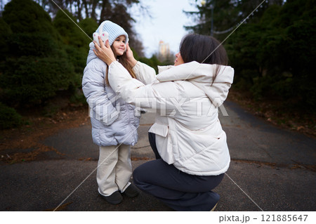 Mother adjusting daughters hat on a chilly day in the park 121885647