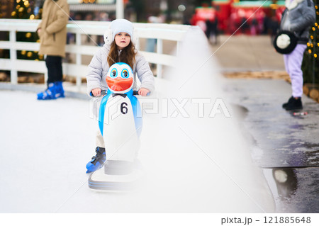 Child enjoying an ice skating experience with a penguin-shaped skating aid 121885648