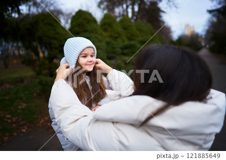 Mother adjusting daughters hat while walking in the park during winter 121885649