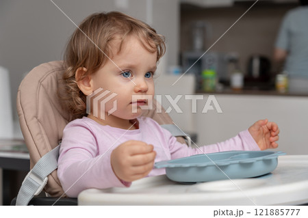 A toddler in a highchair holding a plate while observing the home environment. 121885777