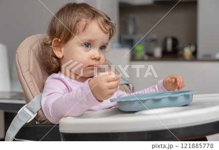 A toddler in a highchair carefully exploring their food in a calm home setting. A toddler in a highchair carefully exploring their food in a calm home setting. 121885778