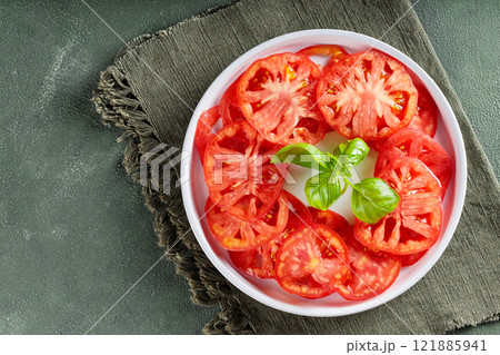 Red Tomato Slices and Fresh Basil Leaves on White Plate with Green Linen Napkin, Copy Space Red Tomato Slices and Fresh Basil Leaves on White Plate with Green Linen Napkin, Copy Space 121885941