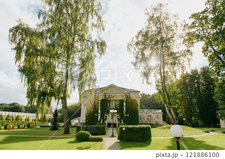 An impressive building is surrounded by trees and grass in a park 121886100